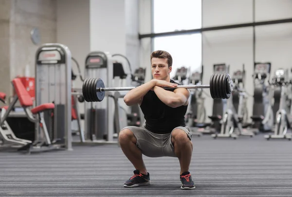 Joven hombre flexionando los músculos con barra en el gimnasio — Foto de Stock