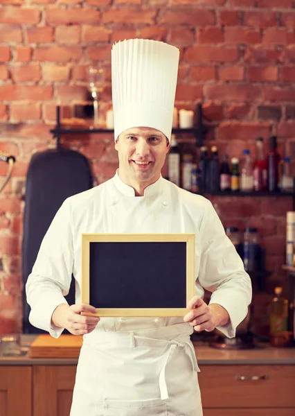 Chef macho feliz com placa de menu em branco na cozinha — Fotografia de Stock