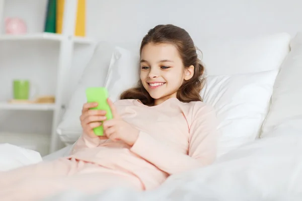 Šťastná dívka leží v posteli s smartphone doma — Stock fotografie