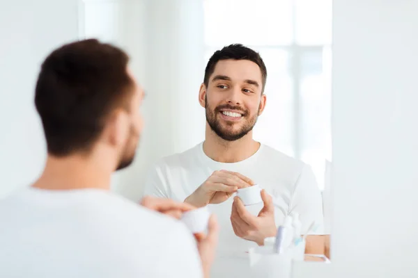 Щасливий молодий чоловік наносить крем обличчям у ванній — стокове фото