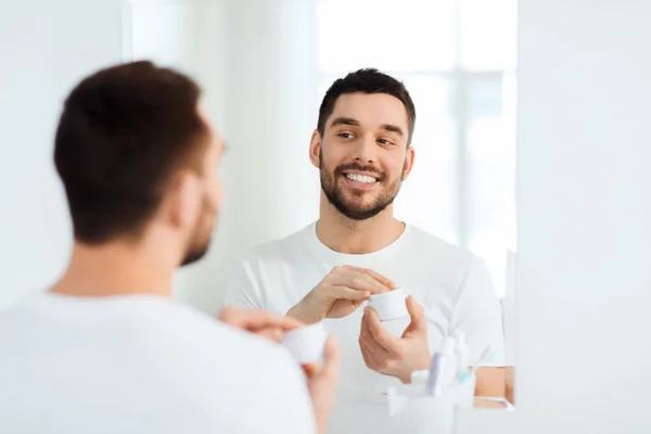 Feliz jovem aplicar creme de rosto no banheiro — Fotografia de Stock