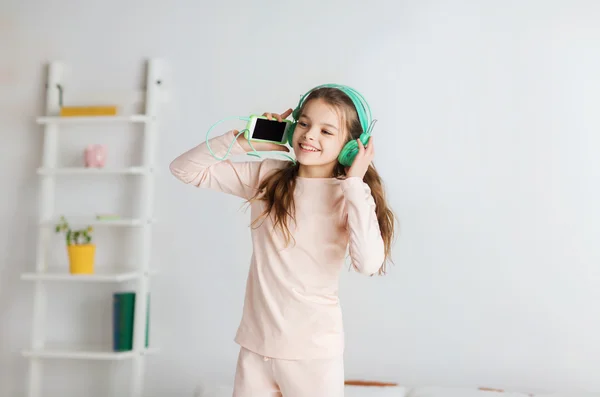 Chica saltando en la cama con teléfono inteligente y auriculares Fotos de stock