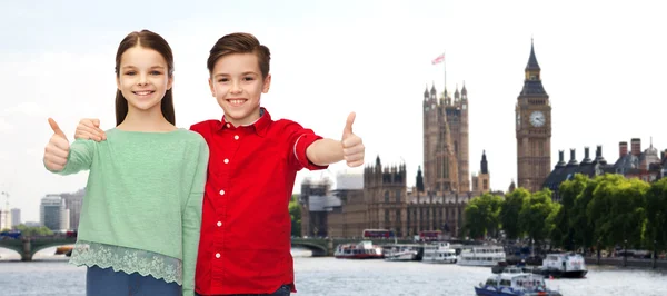Счастливые мальчик и девочка, показывающие большие пальцы вверх над Лондоном — стоковое фото