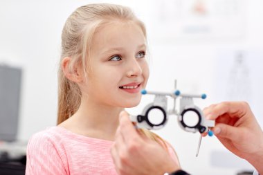 optician with trial frame and girl at clinic clipart