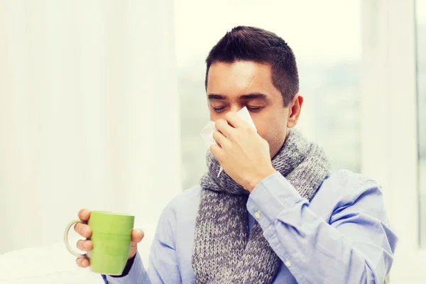 Zieke man met griep drinken thee en blazen neus — Stockfoto