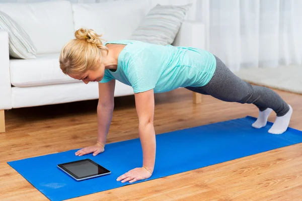 Mulher com tablet pc fazendo exercício prancha em casa — Fotografia de Stock