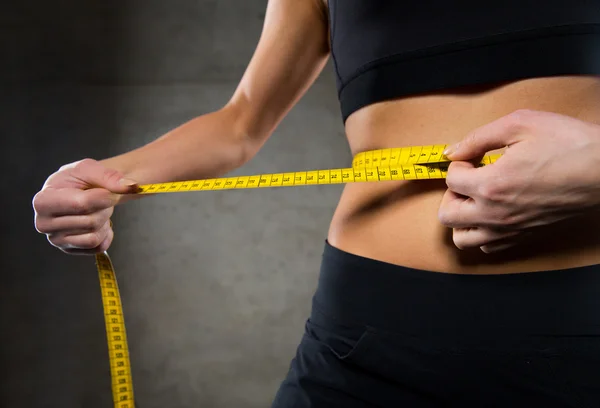 Close up of woman measuring waist by tape in gym — Stock Photo, Image