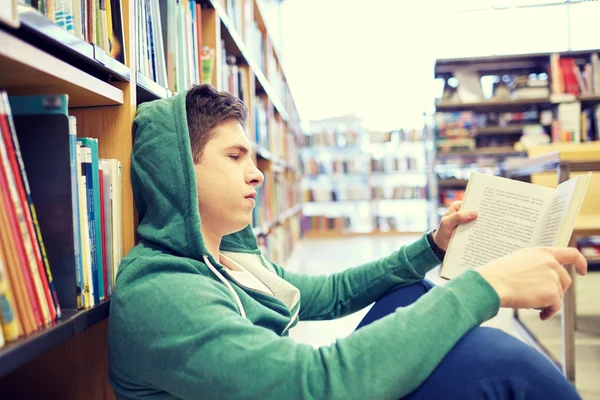 Estudante menino ou jovem leitura livro na biblioteca — Fotografia de Stock