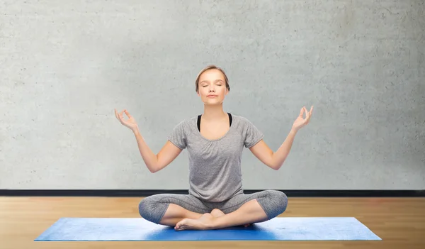 Vrouw maken van yoga meditatie in lotus pose op de mat — Stockfoto