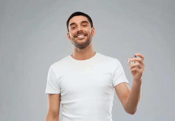 Uomo sorridente con profumo maschile su sfondo grigio — Foto Stock