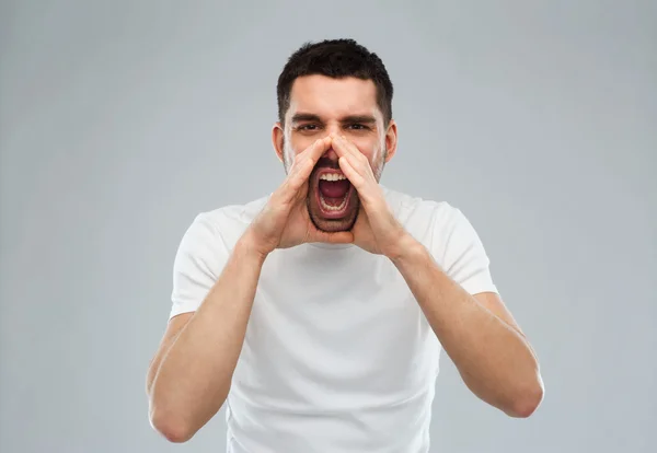 Arrabbiato urlando uomo in t-shirt su sfondo grigio — Foto Stock