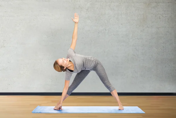 Donna che fa posa triangolo yoga sul tappeto — Foto Stock