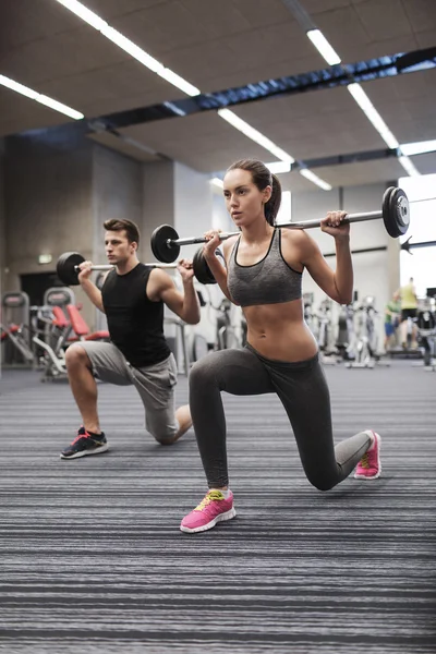 Jonge man en vrouw met barbell in gym training — Stockfoto