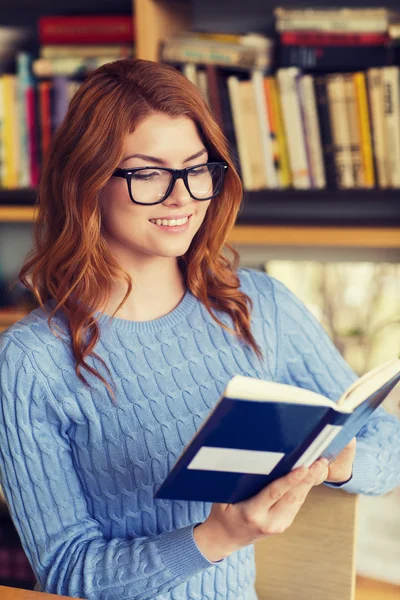 Glückliche Studentin liest Buch in Bibliothek — Stockfoto