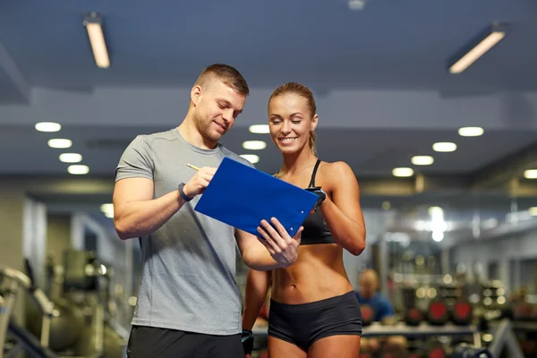 Giovane donna sorridente con personal trainer in palestra — Foto Stock