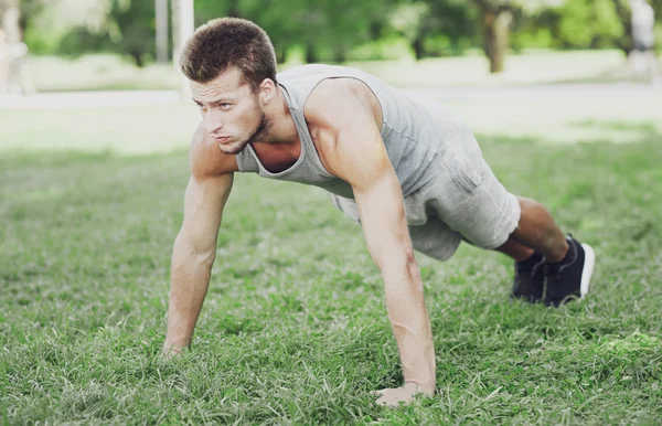 young man doing push ups on grass in summer park