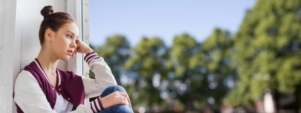 Trauriges hübsches Teenager-Mädchen sitzt auf Fensterbank — Stockfoto