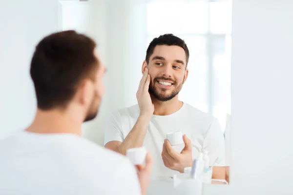 Feliz joven aplicando crema a la cara en el baño —  Fotos de Stock