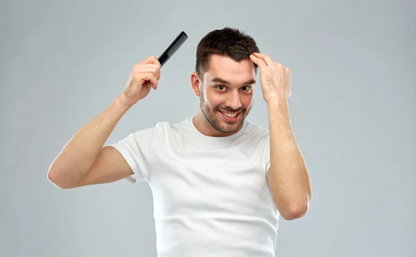 Hombre feliz cepillando el cabello con peine sobre gris — Foto de Stock