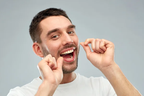 Hombre con hilo dental limpieza de dientes sobre gris —  Fotos de Stock