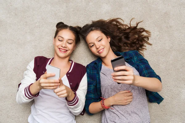 Chicas adolescentes felices tumbadas en el suelo con teléfono inteligente —  Fotos de Stock