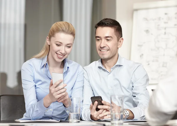 Gente de negocios sonriente con teléfonos inteligentes en la oficina —  Fotos de Stock