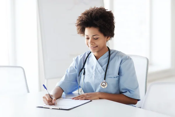 Médico ou enfermeira feliz escrevendo para a área de transferência — Fotografia de Stock