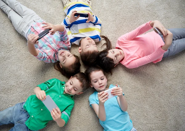 Happy children with smartphones lying on floor — Stock Photo, Image