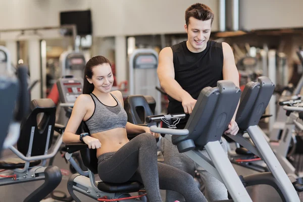 Spor salonunda egzersiz bisikleti üzerinde eğitmen ile mutlu kadın — Stok fotoğraf