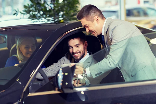 Casal feliz com revendedor de carro em auto show ou salão — Fotografia de Stock