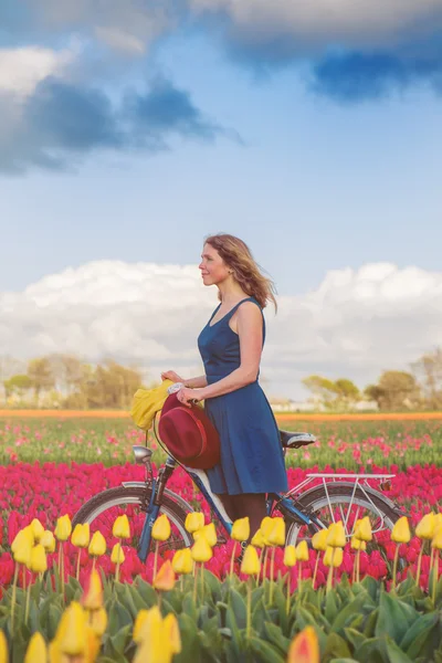 Mujer de pie con su bicicleta en los campos de tulipanes — Foto de Stock