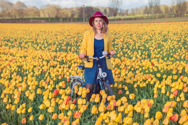 Mujer de pie con su bicicleta en los campos de tulipanes — Foto de Stock