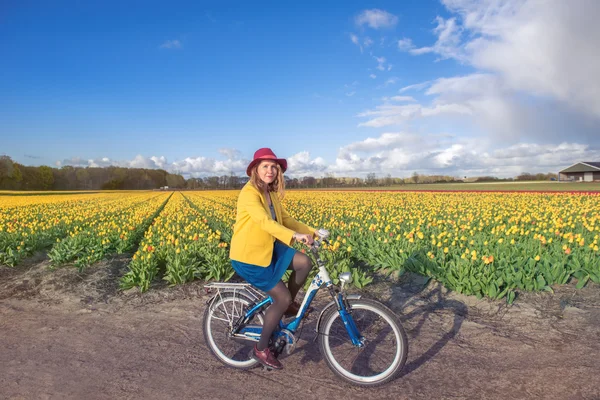 Mulher pedalando ao longo de campos de tulipas — Fotografia de Stock