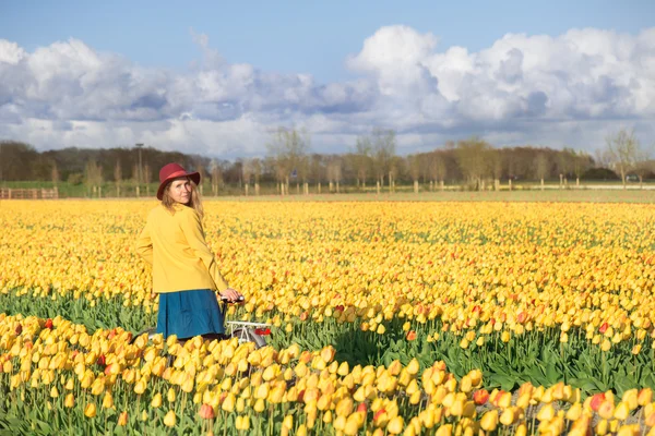 Kvinna som står med sin cykel i tulpaner fält — Stockfoto