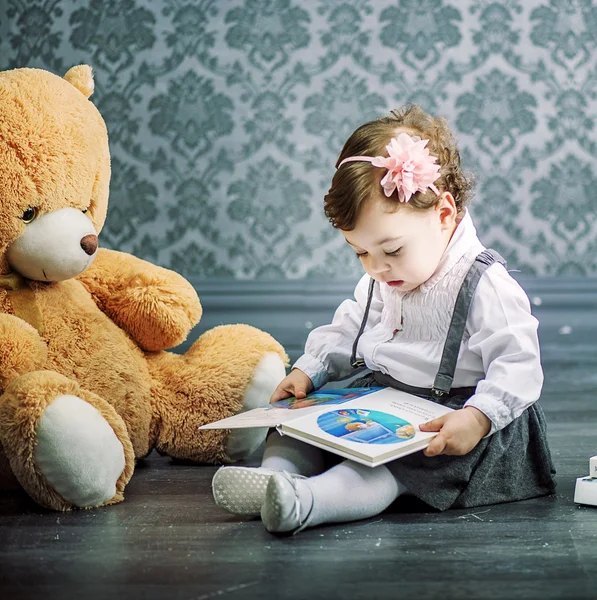 Petite fille mignonne lisant un livre assis sur le sol Image En Vente