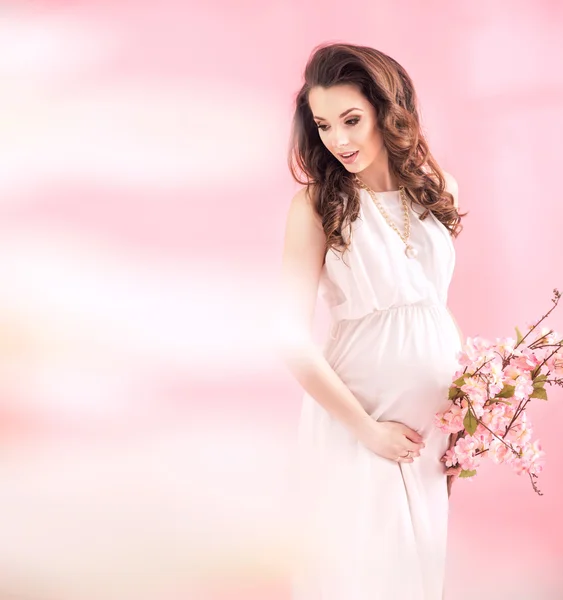 Hermosa mujer embarazada sosteniendo una rama con flores de verano — Foto de Stock