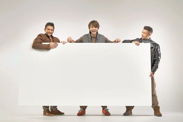 Three cheerful guys holding the board — Stock Photo, Image