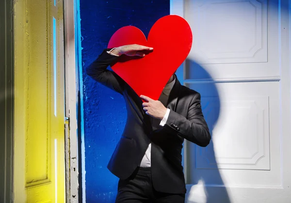 Hombre alegre escondiéndose detrás de un corazón — Foto de Stock