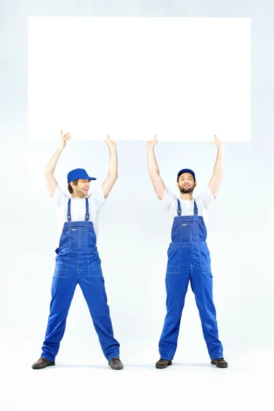 Twee knappe bouwers houden een bord — Stockfoto