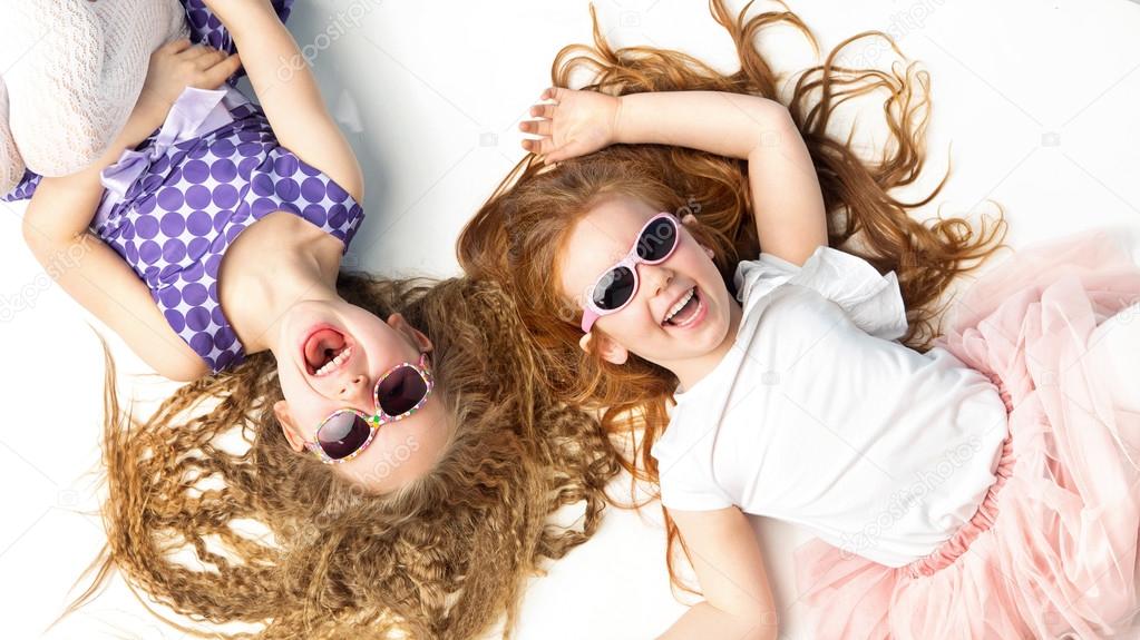 Two laughing girls lying on a white floor