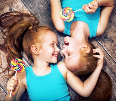 Fine portrait of a twin sisters holding lollipops
