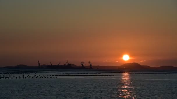 Zeitraffer des Sonnenuntergangs auf See mit dem Hintergrund des Frachthafens — Stockvideo