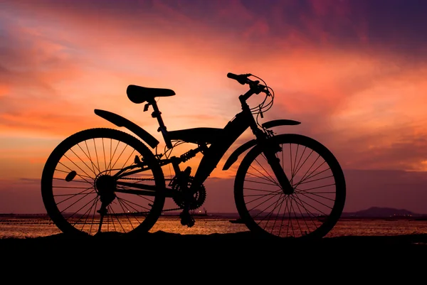 Silhouette of mountain bike parking on jetty beside sea with sun — Stock Photo, Image