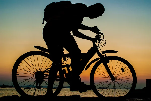 Silhouette of backpacker ride mountain bike on bridge beside sea — Stock Photo, Image