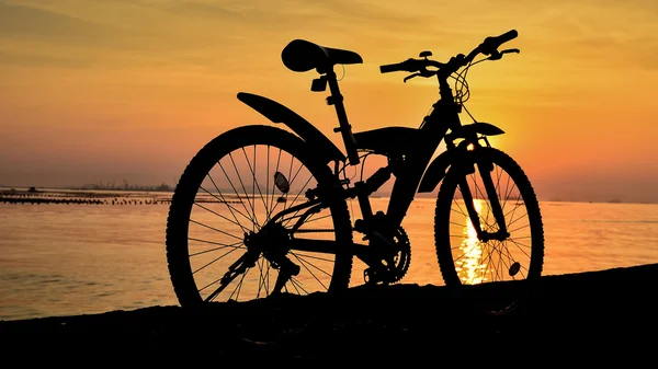 Silhouet van mountainbike parkeren op steiger naast zee met zon — Stockfoto