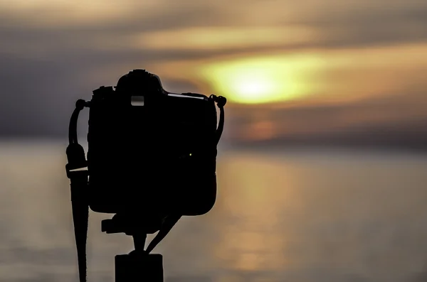 Силуэт цифровой камеры у моря на закате — стоковое фото