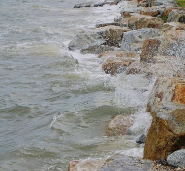 Dalgalar sahildeki kayalara çarpar, yakın çekim.