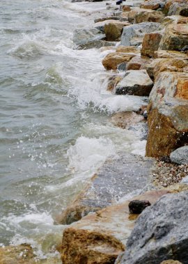 Dalgalar sahildeki kayalara çarpar, yakın çekim.