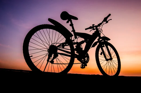 Silhouette of mountain bike parking on jetty beside sea with sun — Stock Photo, Image