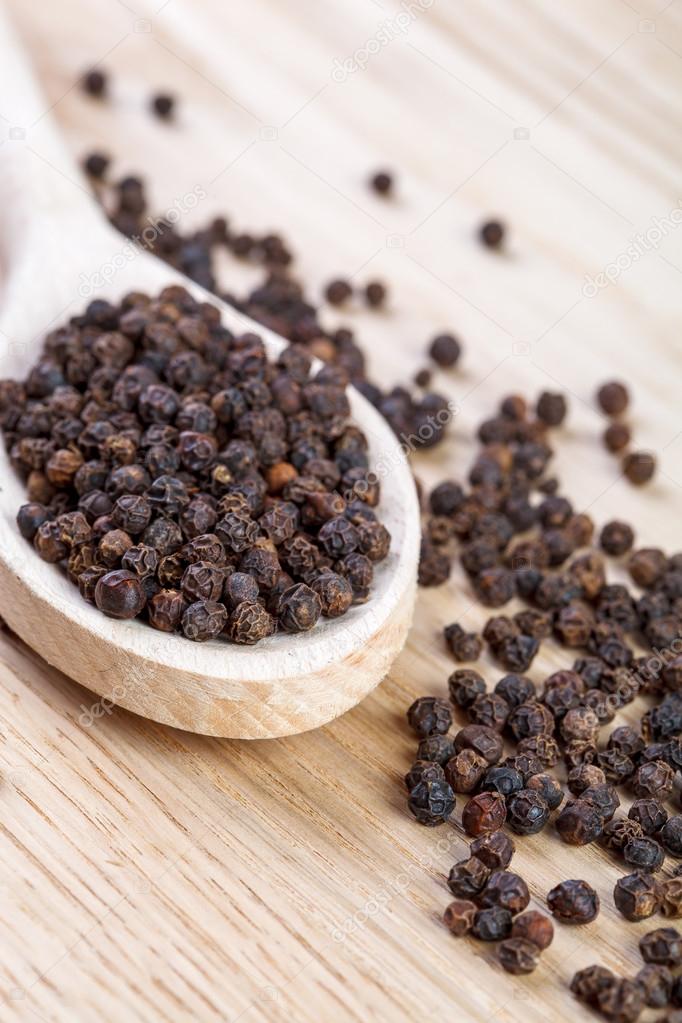 Black pepper on wooden spoon close up